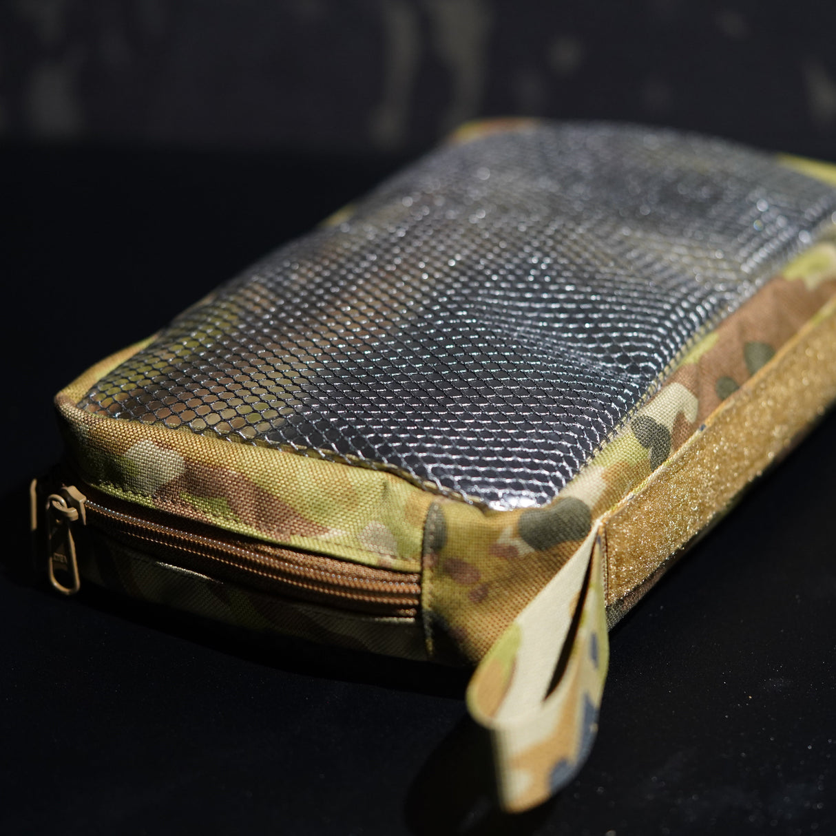 Camouflage-patterned pouch with a zipper on a dark background